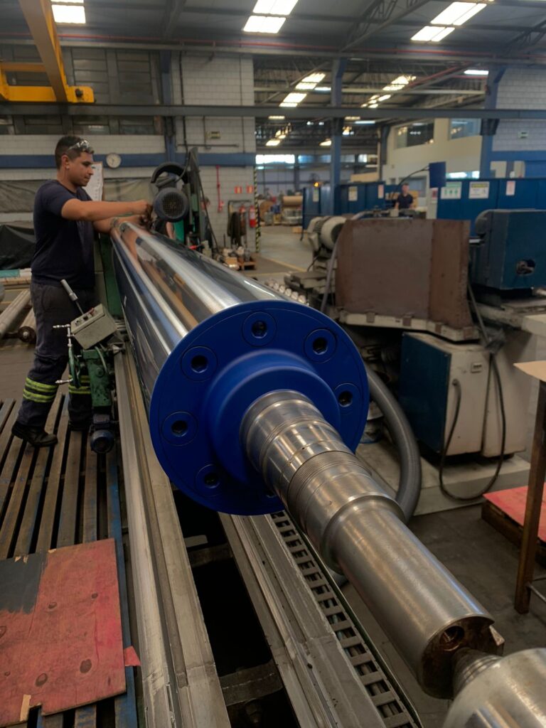 Trabalhador trabalhando com rolo guia utilizado na indústria de papel e celulose, revestido com a liga SULFORM para aumentar a vida útil, reduzir custos de manutenção e garantir a qualidade do papel produzido.